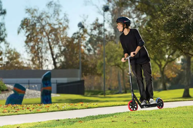 young man enjoys riding on his razor a5 lux scooter while roaming around the park