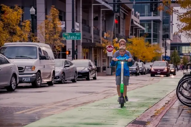 Two boys riding lime scooter on street